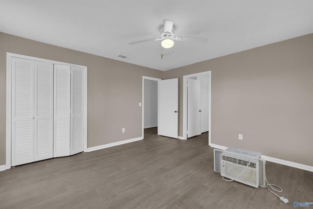 unfurnished bedroom featuring visible vents, baseboards, a ceiling fan, wood finished floors, and a wall mounted air conditioner