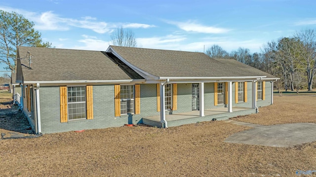 rear view of property with covered porch, brick siding, and roof with shingles