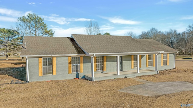 rear view of property featuring a shingled roof, a porch, and brick siding