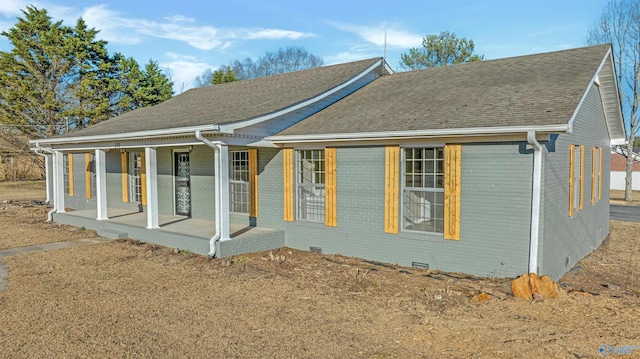 exterior space featuring crawl space, covered porch, roof with shingles, and brick siding