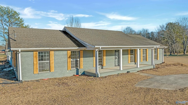 back of house with a porch, roof with shingles, and brick siding