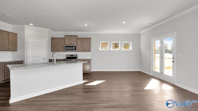 kitchen with dark hardwood / wood-style flooring, a kitchen island with sink, crown molding, light stone countertops, and appliances with stainless steel finishes