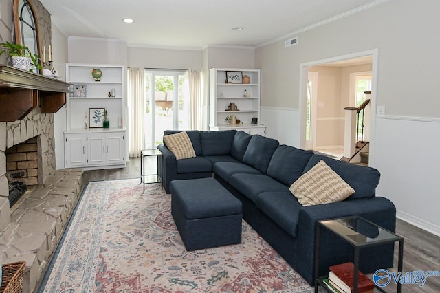 living room with ornamental molding, a stone fireplace, and wood-type flooring