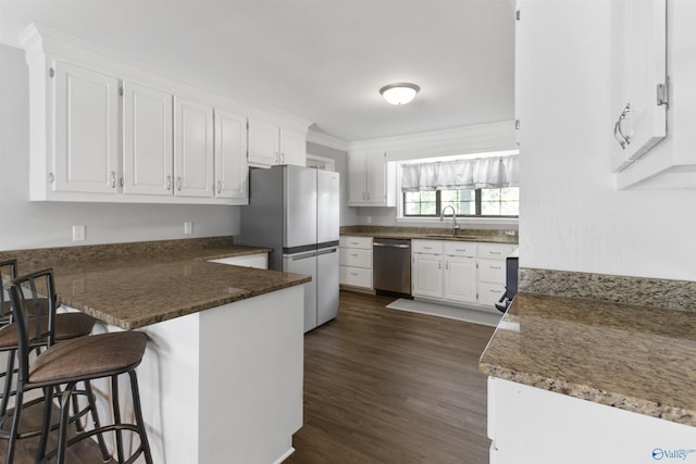 kitchen with white cabinetry, a sink, appliances with stainless steel finishes, and a peninsula
