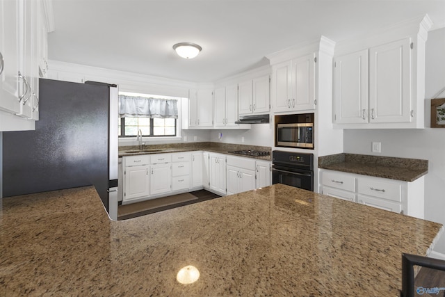 kitchen featuring a sink, white cabinetry, under cabinet range hood, stainless steel appliances, and dark stone counters