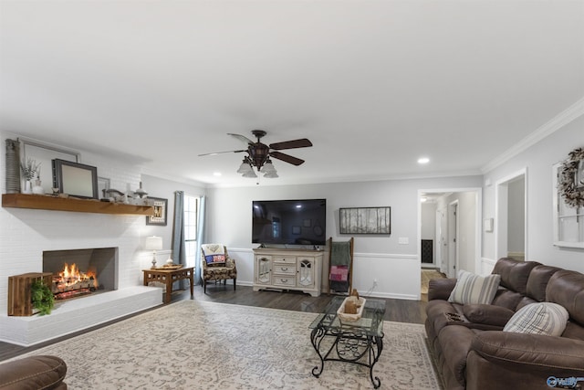 living area featuring a brick fireplace, crown molding, dark wood-type flooring, and a ceiling fan