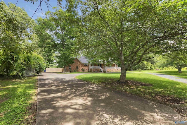 view of front of home featuring driveway, a front yard, fence, brick siding, and a porch