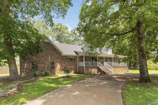 view of front of property featuring concrete driveway, brick siding, a front lawn, a shingled roof, and a porch