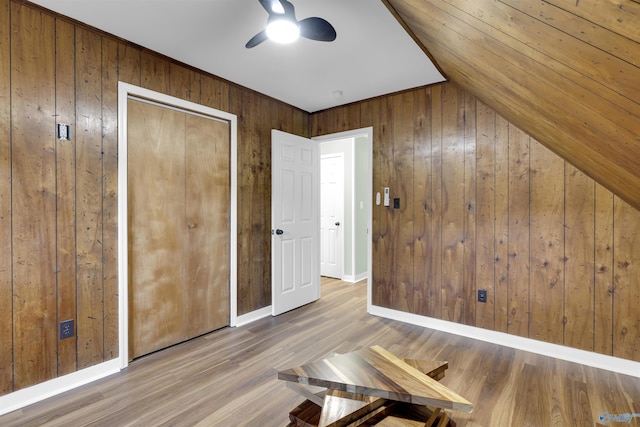 unfurnished bedroom featuring wooden walls, vaulted ceiling, wood-type flooring, and ceiling fan