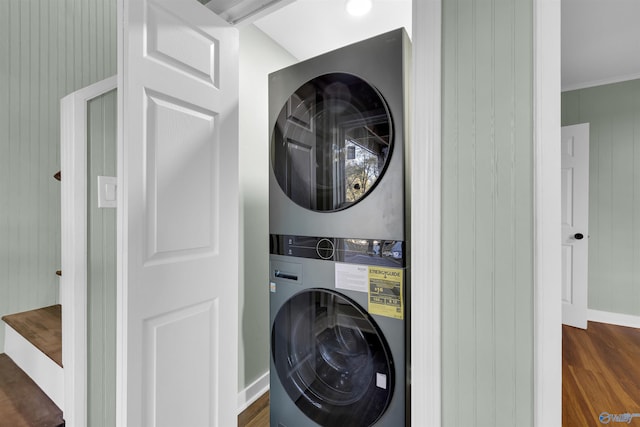 laundry room featuring stacked washer / dryer, wood walls, ornamental molding, and dark hardwood / wood-style floors