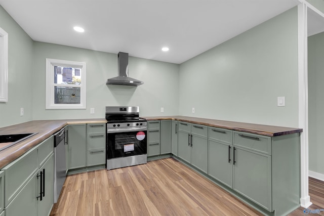 kitchen featuring wall chimney range hood, butcher block counters, appliances with stainless steel finishes, and light hardwood / wood-style floors