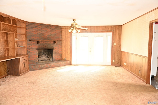 unfurnished living room featuring light carpet, wooden walls, a fireplace, and ceiling fan