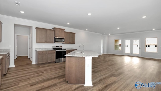 kitchen with light stone counters, dark hardwood / wood-style floors, a center island with sink, appliances with stainless steel finishes, and ornamental molding