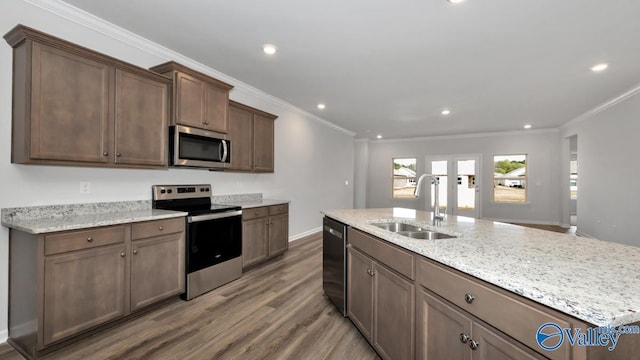 kitchen with ornamental molding, stainless steel appliances, a kitchen island with sink, sink, and wood-type flooring