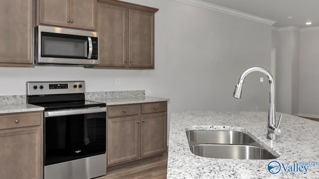 kitchen with sink, hardwood / wood-style flooring, light stone countertops, ornamental molding, and appliances with stainless steel finishes