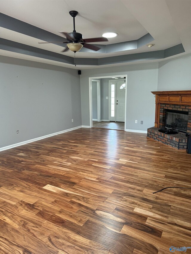 103 Katelyn Dr, Meridianville, AL 35759 - unfurnished living room with dark wood-type flooring, a tray ceiling, ceiling fan, and a fireplace