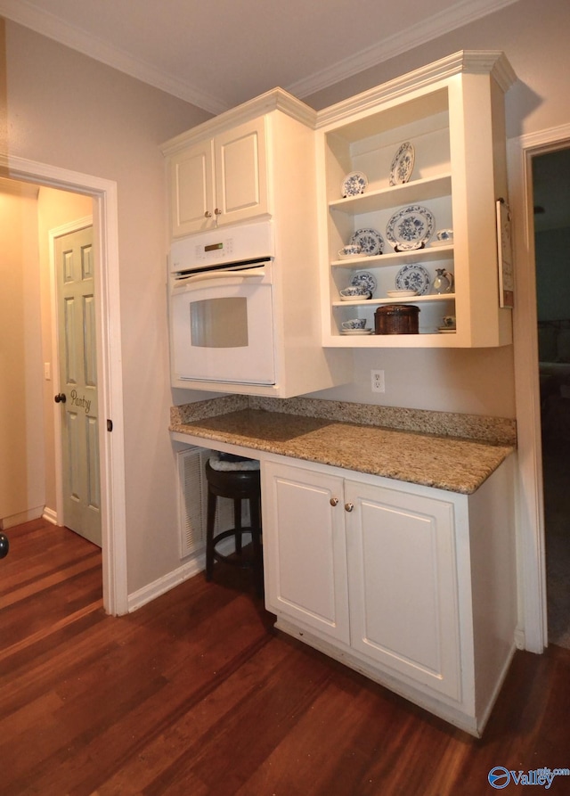 kitchen featuring white cabinets, oven, dark hardwood / wood-style floors, light stone countertops, and ornamental molding