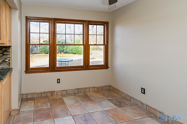 unfurnished room featuring a ceiling fan, baseboards, a textured ceiling, and stone tile floors