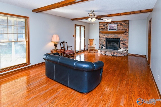 living room with a brick fireplace, beamed ceiling, baseboards, and wood finished floors