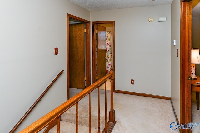 hall with carpet floors, baseboards, a textured ceiling, and an upstairs landing