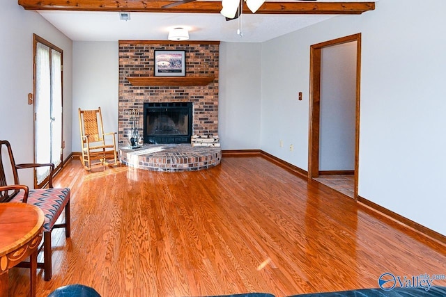 unfurnished living room featuring wood finished floors, visible vents, baseboards, a brick fireplace, and beam ceiling