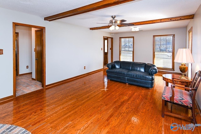 living area with a textured ceiling, wood finished floors, a ceiling fan, baseboards, and beam ceiling