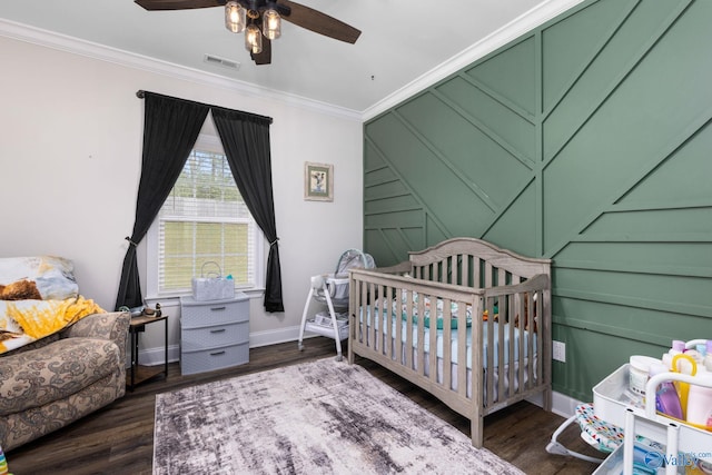 bedroom featuring dark wood-type flooring, a nursery area, ceiling fan, and crown molding