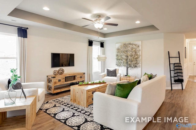 living room with ceiling fan, a raised ceiling, and wood-type flooring