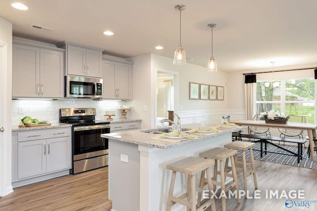 kitchen featuring light wood finished floors, tasteful backsplash, gray cabinets, appliances with stainless steel finishes, and a sink