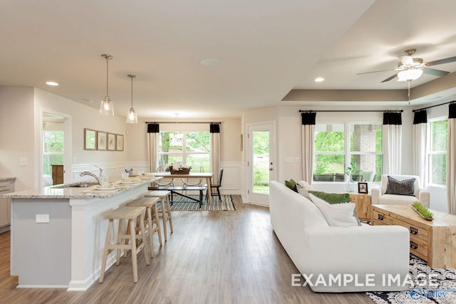 kitchen featuring light wood-style floors, wainscoting, a sink, light stone countertops, and a kitchen bar