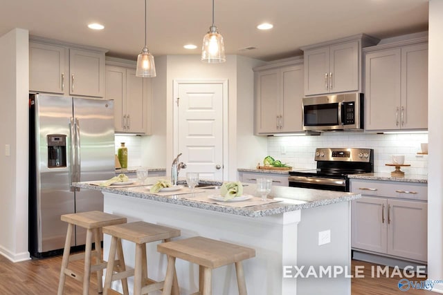 kitchen with light stone counters, stainless steel appliances, gray cabinetry, a kitchen island with sink, and a kitchen bar