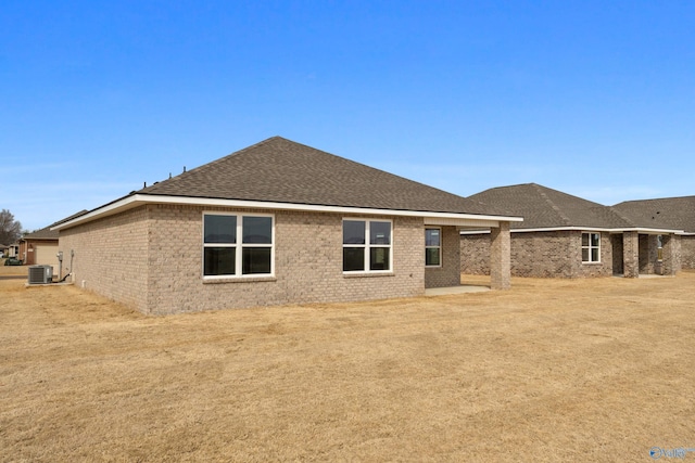 rear view of house with a shingled roof, central AC, and brick siding