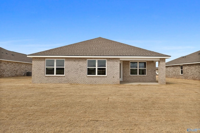 rear view of property with roof with shingles, a lawn, a patio, and brick siding