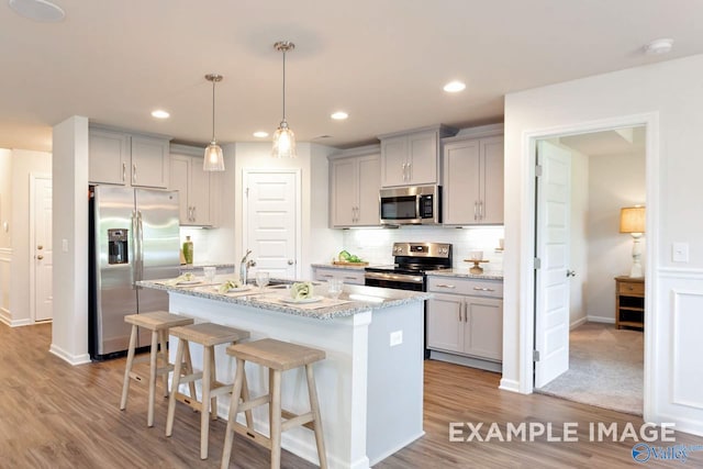 kitchen featuring light wood-type flooring, a kitchen breakfast bar, a center island with sink, appliances with stainless steel finishes, and light stone countertops