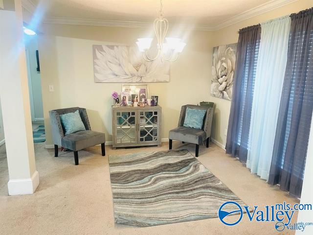 living area with a chandelier, carpet, and ornamental molding