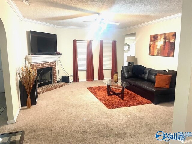 carpeted living room with a textured ceiling, ornamental molding, a brick fireplace, and ceiling fan