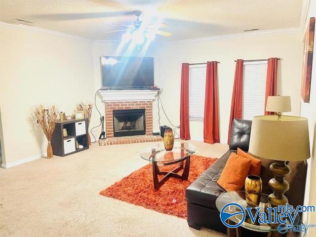 carpeted living room with a brick fireplace, crown molding, and ceiling fan