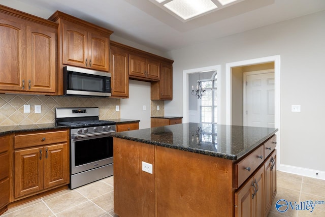 kitchen with light tile patterned flooring, a kitchen island, stainless steel appliances, dark stone counters, and an inviting chandelier