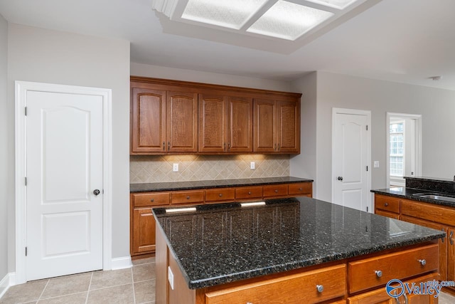 kitchen with sink, a center island, dark stone countertops, decorative backsplash, and light tile patterned floors