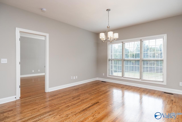 empty room featuring wood-type flooring and an inviting chandelier