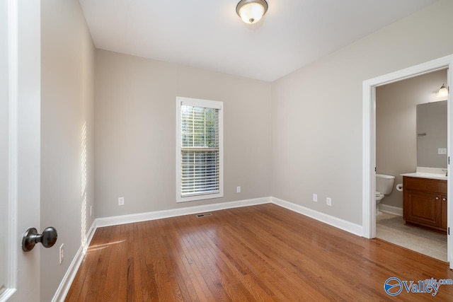 unfurnished bedroom featuring hardwood / wood-style flooring and connected bathroom