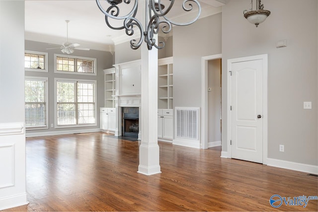 unfurnished living room with decorative columns, dark wood-type flooring, ceiling fan with notable chandelier, a towering ceiling, and crown molding