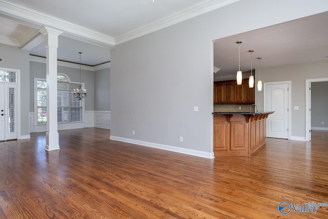 unfurnished living room with sink, decorative columns, dark hardwood / wood-style flooring, crown molding, and a notable chandelier