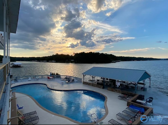 pool at dusk featuring a water view, a patio area, and a gazebo