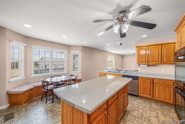 kitchen with ceiling fan, sink, light stone counters, stainless steel dishwasher, and a kitchen island