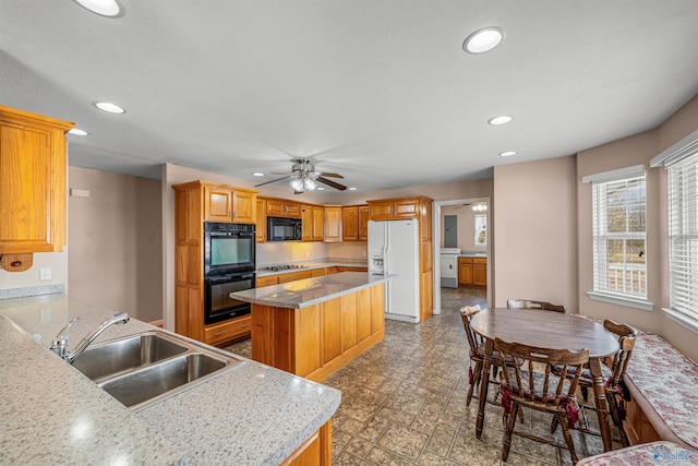 kitchen with ceiling fan, sink, a center island, washer / dryer, and black appliances