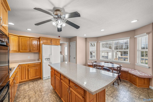 kitchen featuring ceiling fan, white fridge with ice dispenser, a center island, oven, and a textured ceiling