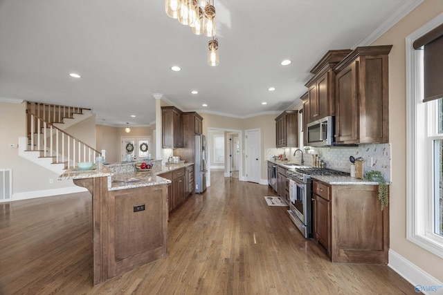 kitchen featuring stainless steel appliances, a peninsula, baseboards, and a sink