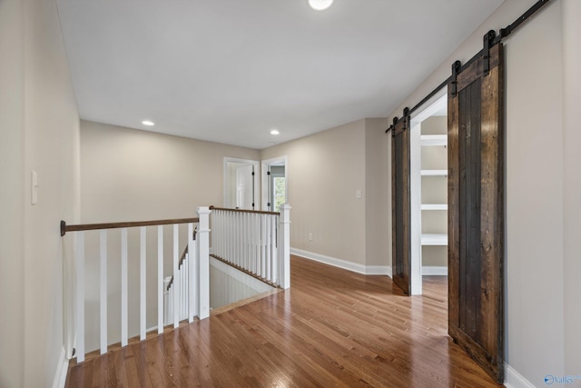 hallway with baseboards, a barn door, an upstairs landing, recessed lighting, and wood finished floors