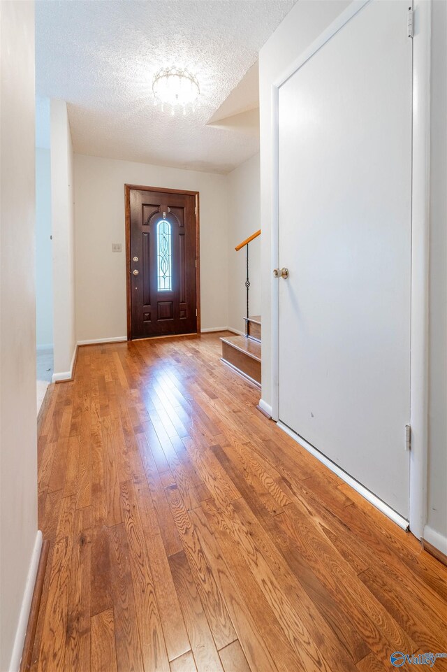 foyer featuring baseboards, a textured ceiling, and wood finished floors